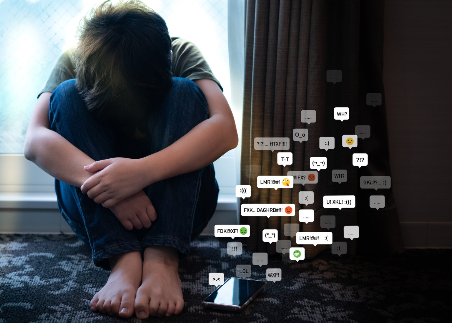 Portrait of a teenager boy sitting alone in the room with his smartphone, feeling hurt, anxiety and depress from cyberbullying on social media. Technology and mental health problems with children concept.